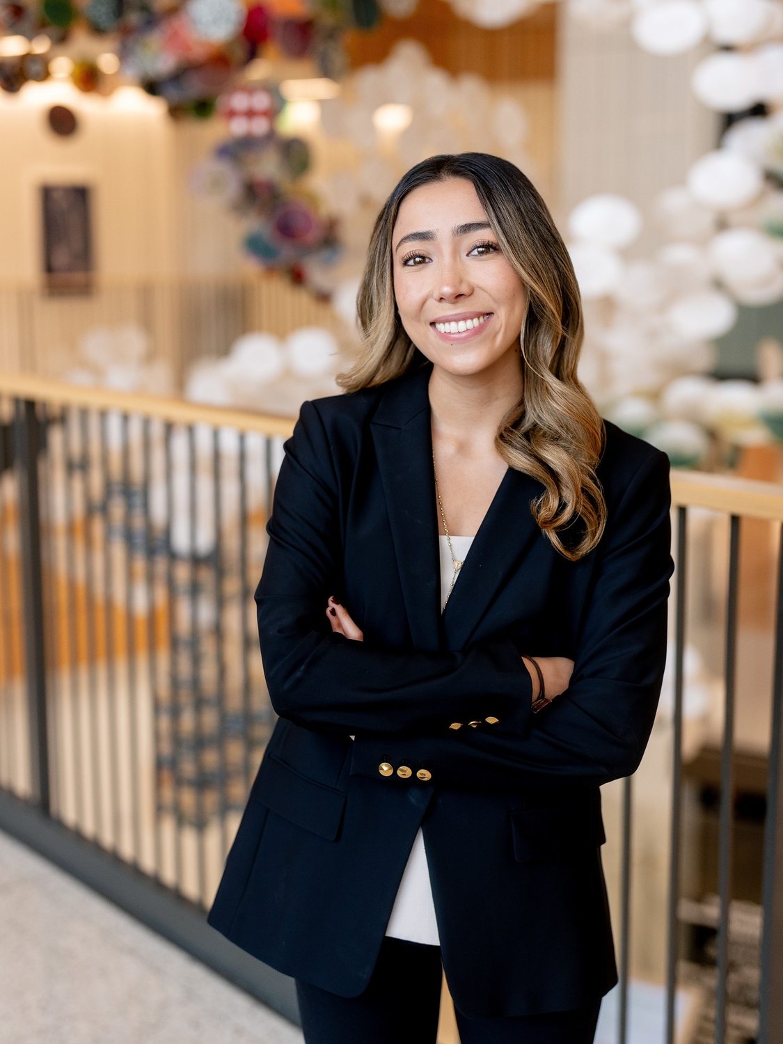 María in a black blazer, arms crossed, smiling by a railing