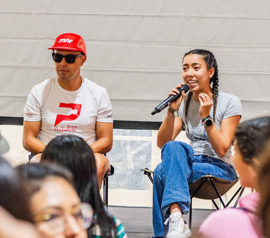 María on stage with a microphone next to a team athlete at Oceanman Guatapé