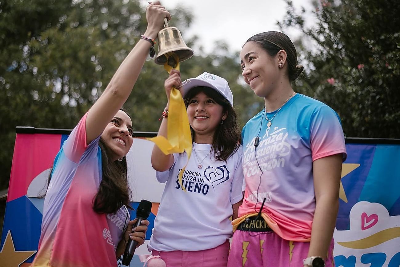A girl from the foundation ringing the bell on stage, María beside her