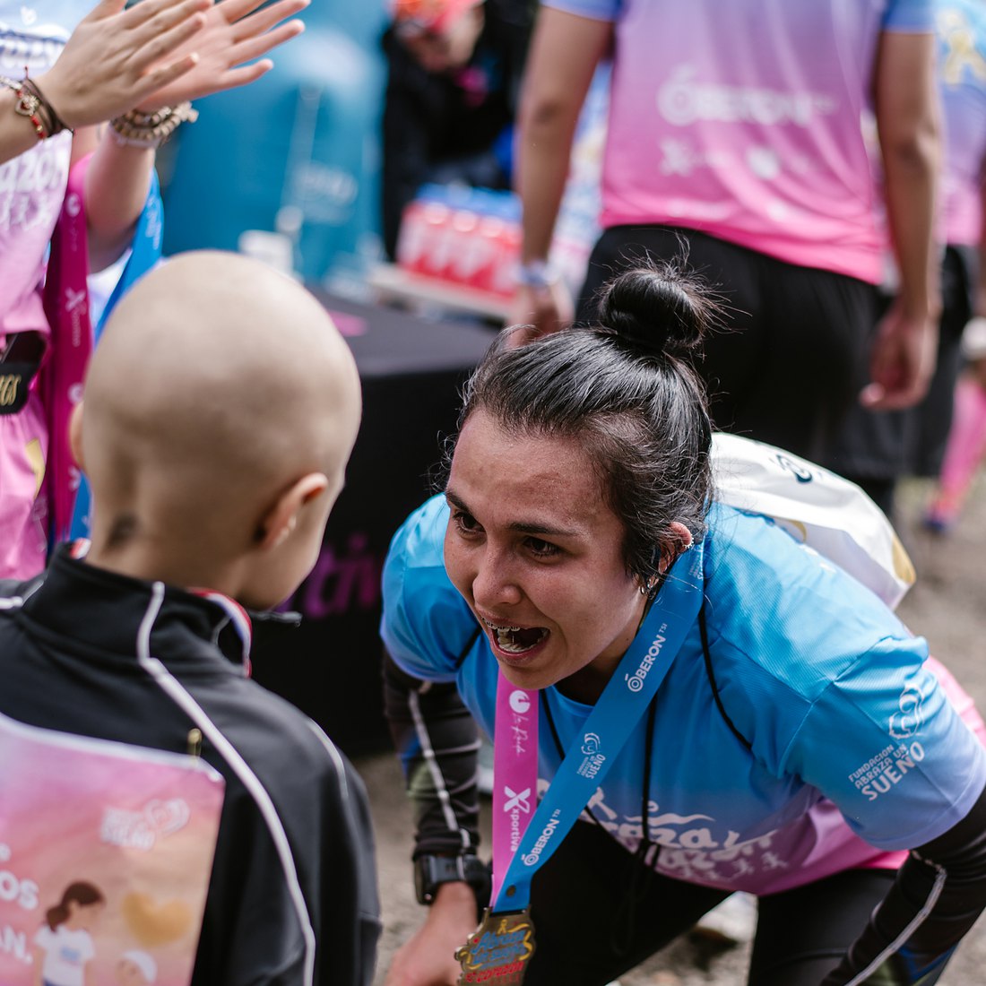 A child from the foundation putting the finisher medal on a runner, who crouches down, moved