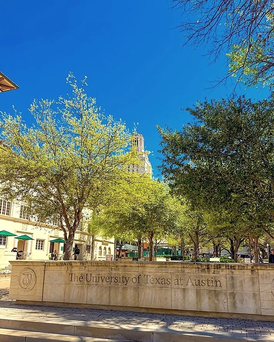 The University of Texas at Austin stone sign under spring trees, the UT Tower behind